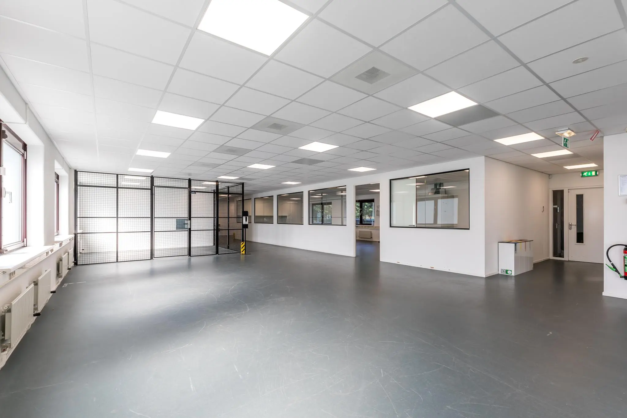 Ruime, moderne bedrijfsruimte aan de Baarnsche Dijk met systeemplafond, grote ramen en een afgesloten gaaswand.